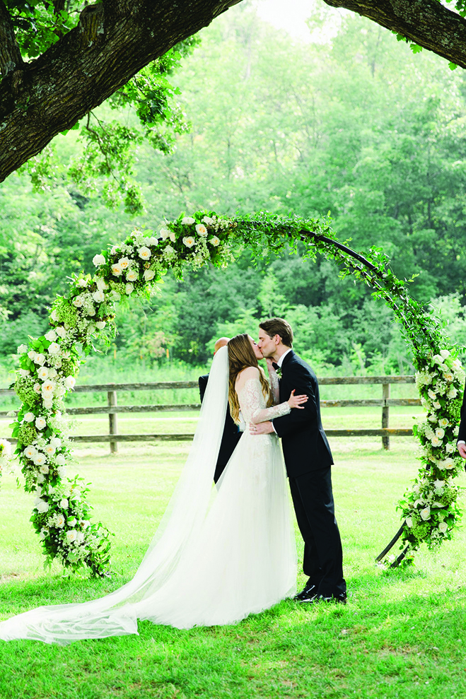 Laura and Rob kiss under a round arch at Mayowood Stone Barn