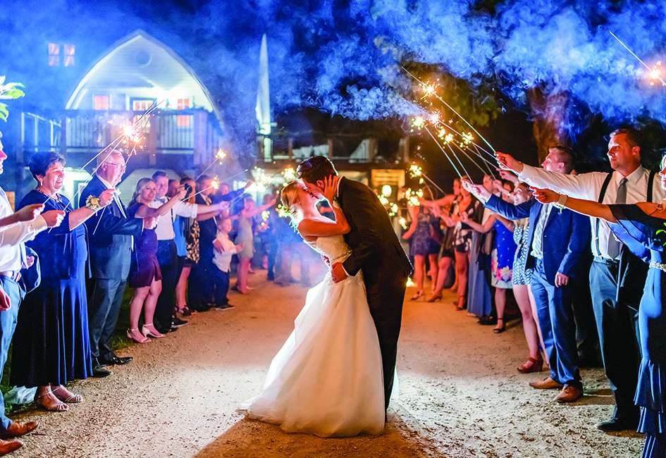 Family and friends hold sparklers as Taylor and John kiss as their wedding day at Historic John P. Furber Farm ends.