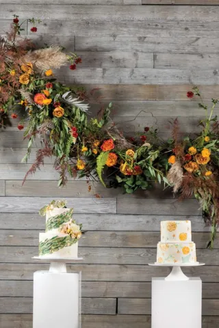 A playful installation of ranunculus, roses, olive branches and ferns frolics across the wall behind an array of autumn-inspired cakes at Machine Shop.