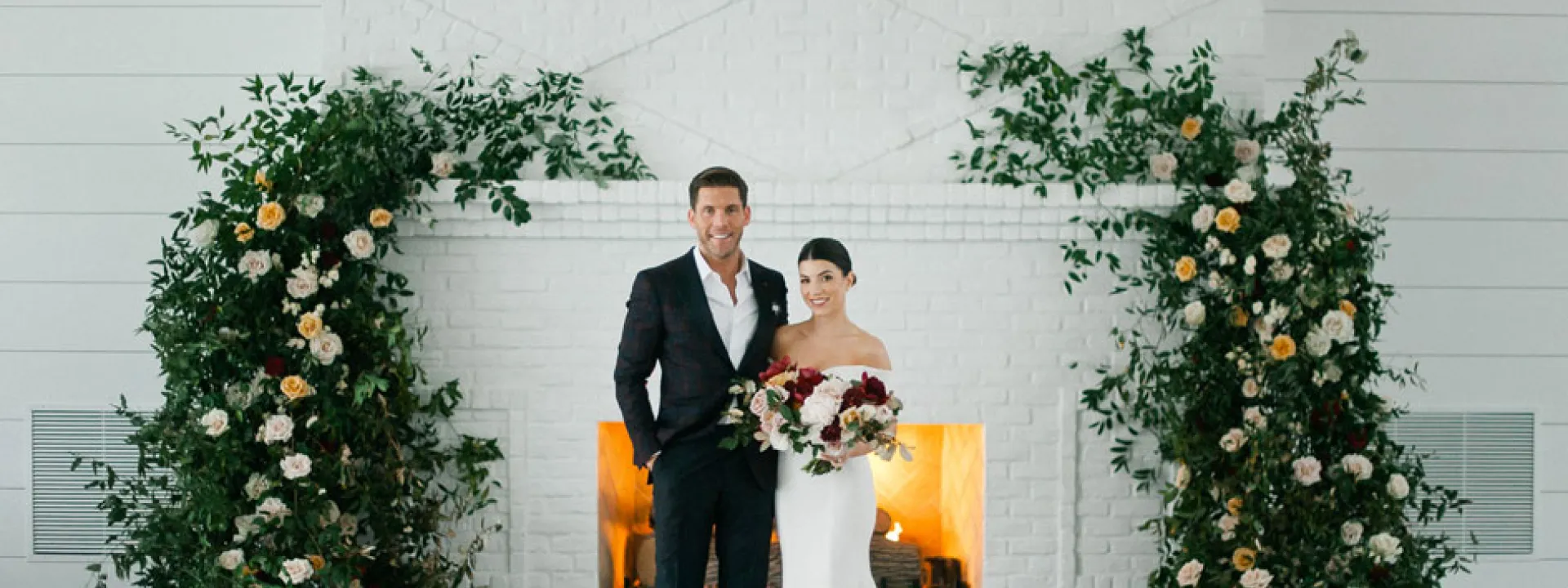 Sydney and Casey pose before the beautiful fireplace and their rosy floral installation at Hutton House