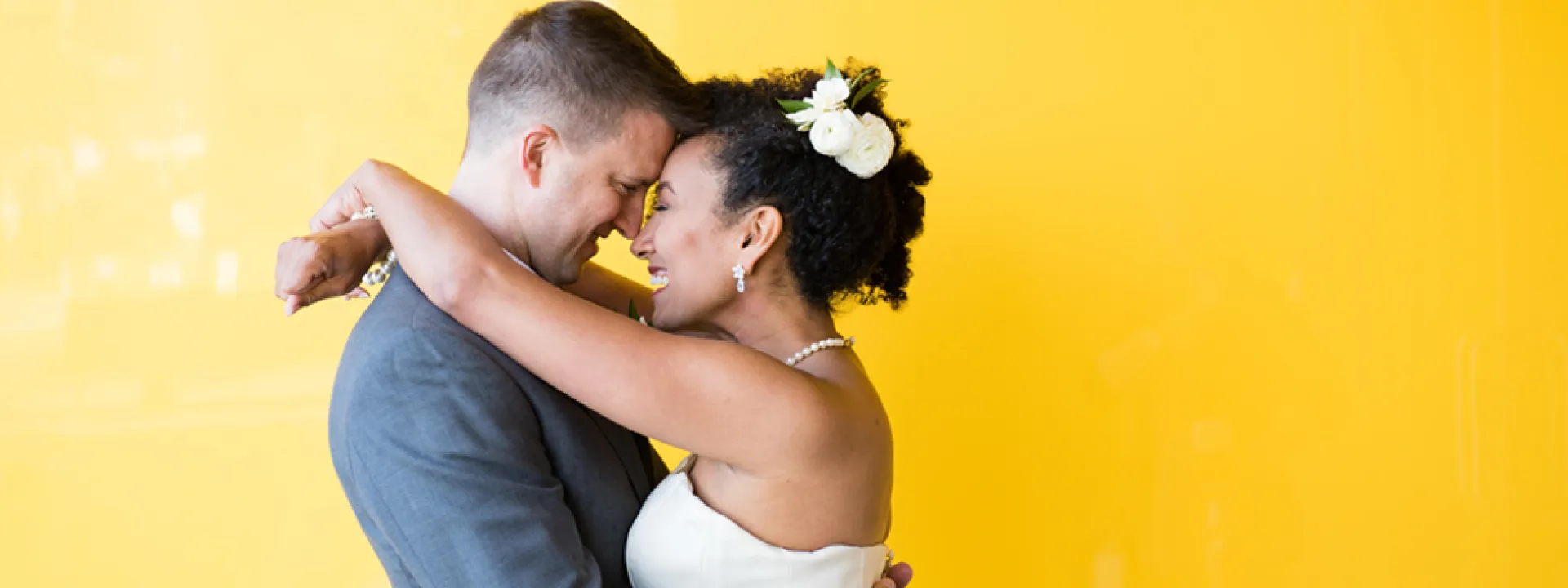 Newlywed couple happily hugging in front of a bright yellow accent wall at Walker Art Center. 